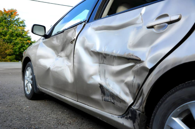 A silver car with a damaged door is parked on the side of the road.