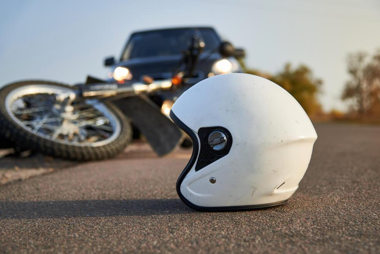 A helmet is laying on the ground next to a motorcycle that has crashed into a car.