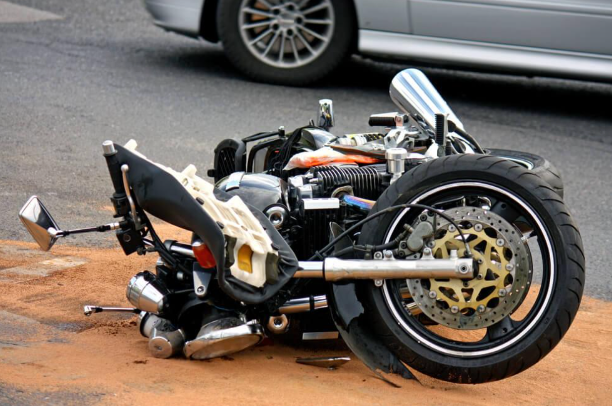 A motorcycle is laying on the ground next to a car.
