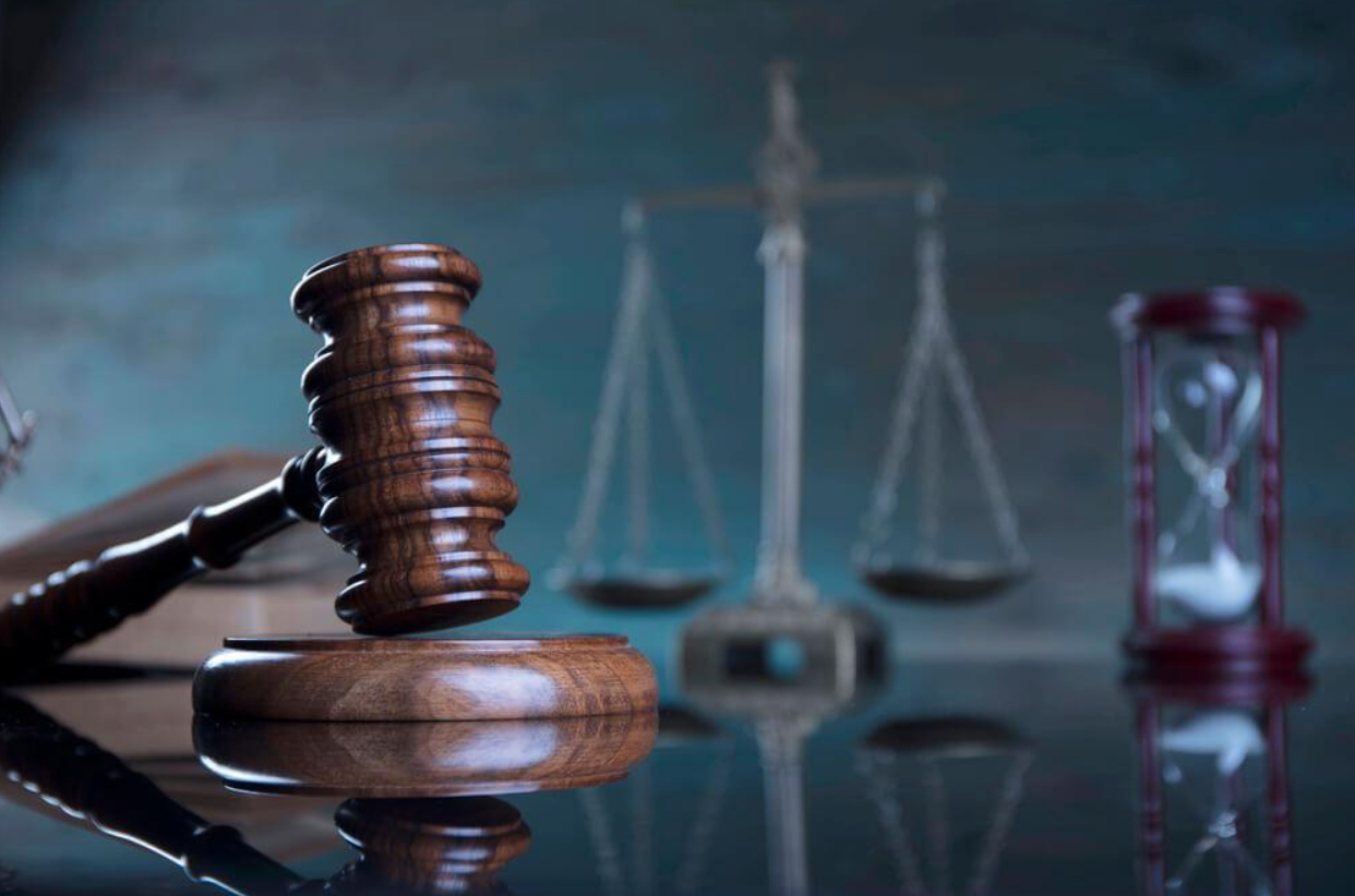 A wooden judge 's gavel is sitting on a table in front of a scale of justice and an hourglass.