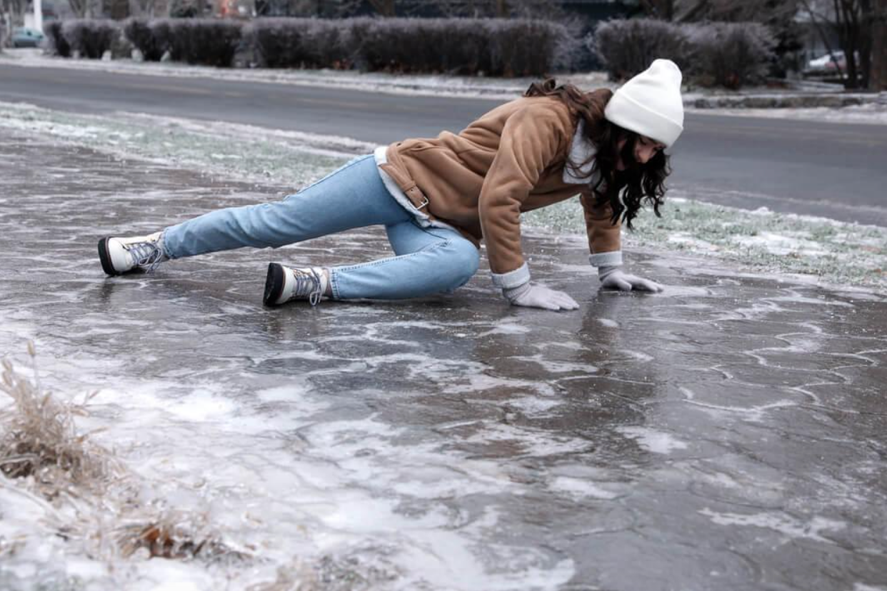 A woman is crawling on the ice on the sidewalk.