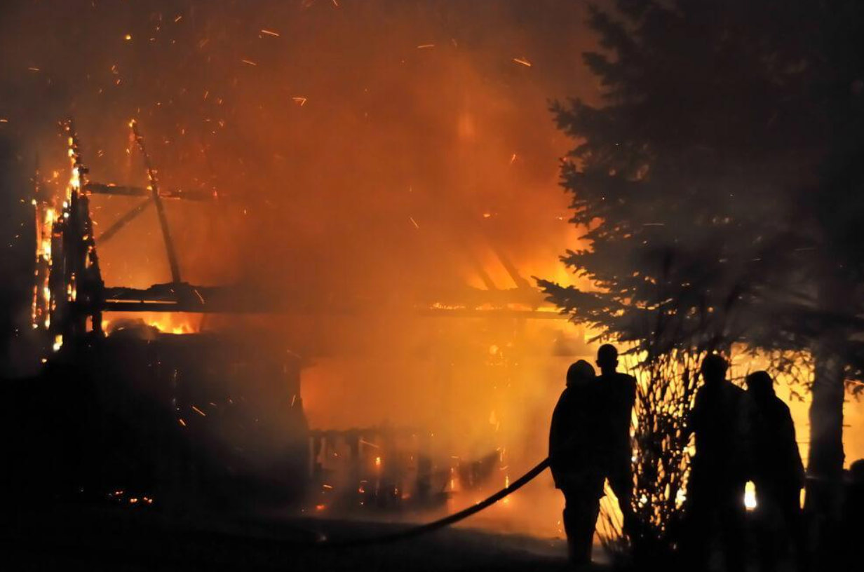 A group of firefighters are standing in front of a large fire.