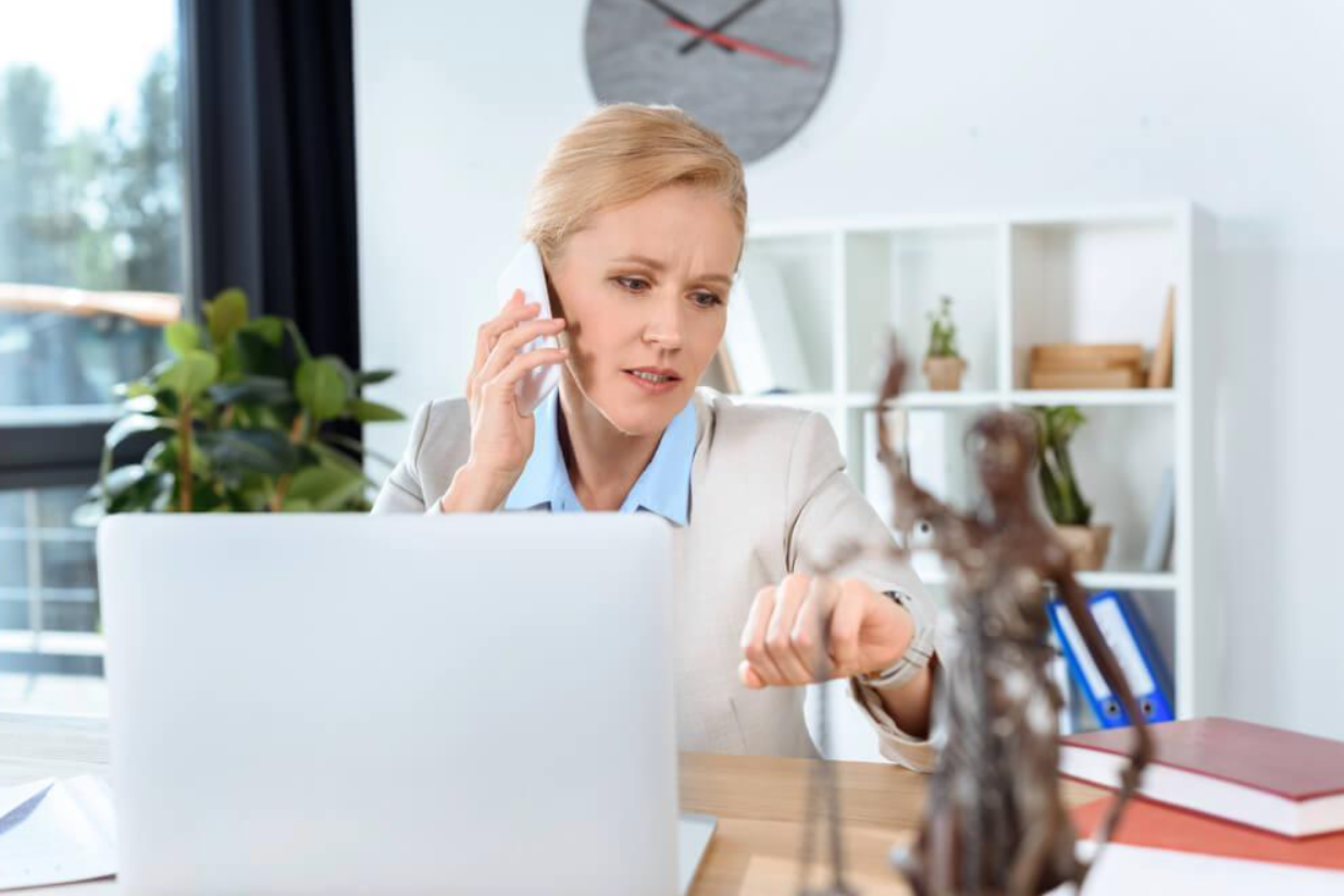 A woman is sitting at a desk talking on a cell phone in front of a laptop computer.