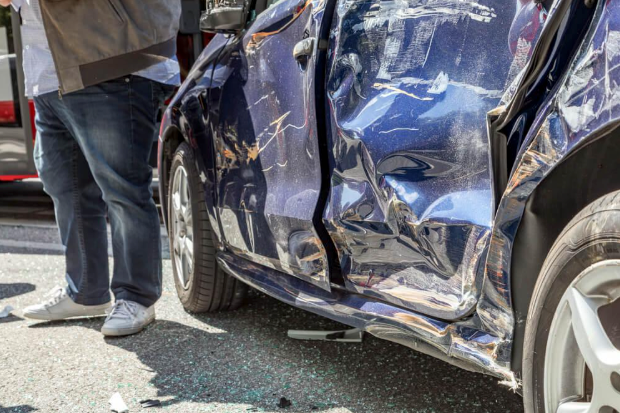 A man is standing next to a damaged blue car.
