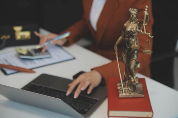 A woman is sitting at a desk with a laptop and a statue of justice.