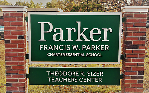 A sign for the Francis W. Parker Charter Essential School and Theodore R. Sizer Teachers Center, mounted between brick pillars.