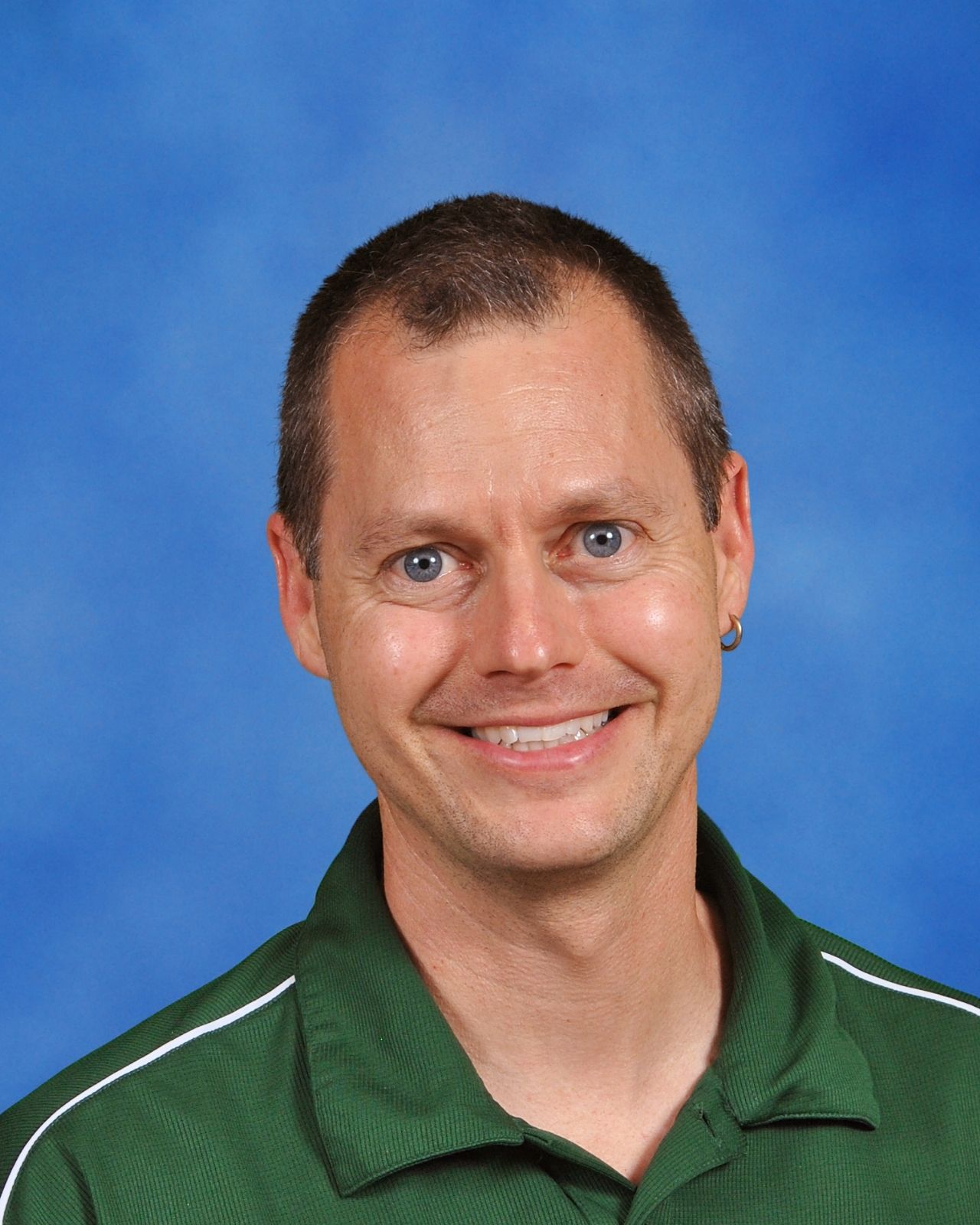 A smiling man with short hair wearing a green polo shirt against a blue background.