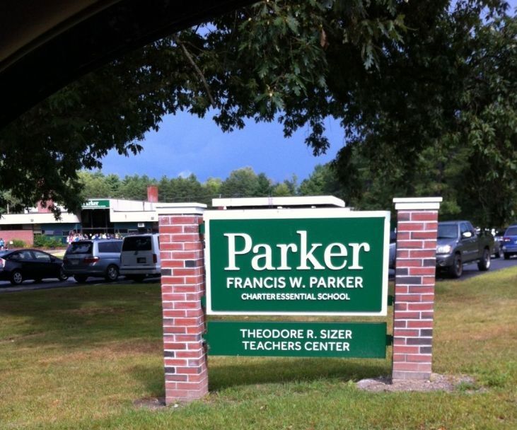 A green sign for the Francis W. Parker Charter Essential School and Theodore R. Sizer Teachers Center on brick pillars.