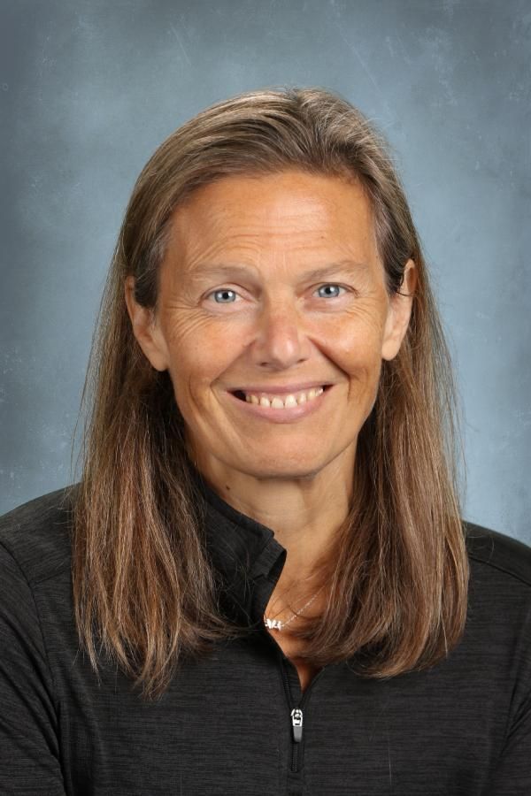 Portrait of a smiling person with shoulder-length brown hair, wearing a black quarter-zip shirt against a blue background.
