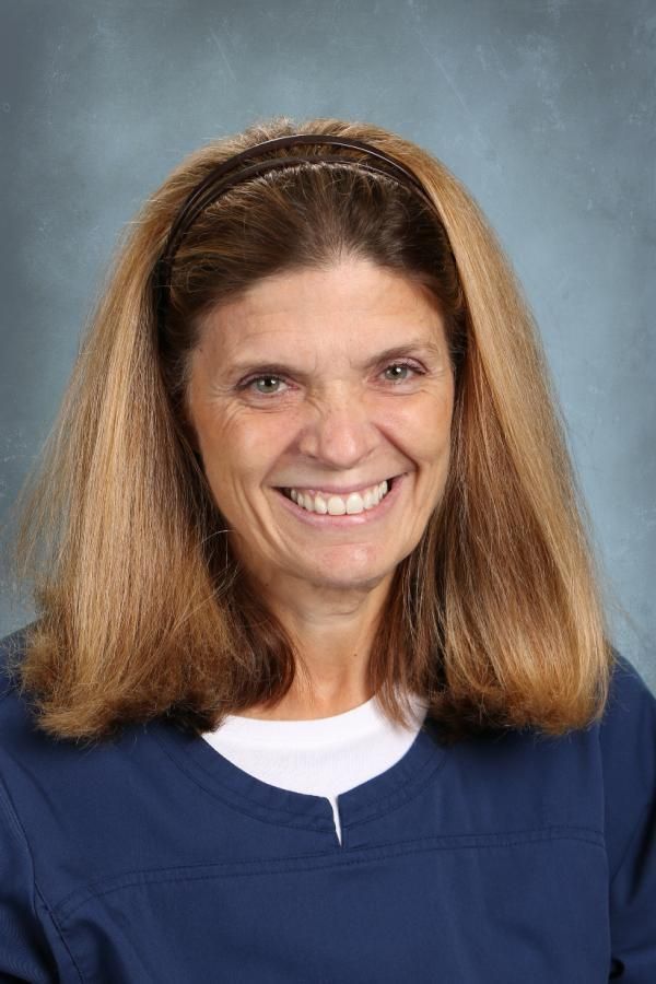 A smiling person with long light brown hair wearing a dark blue top, against a blue background.