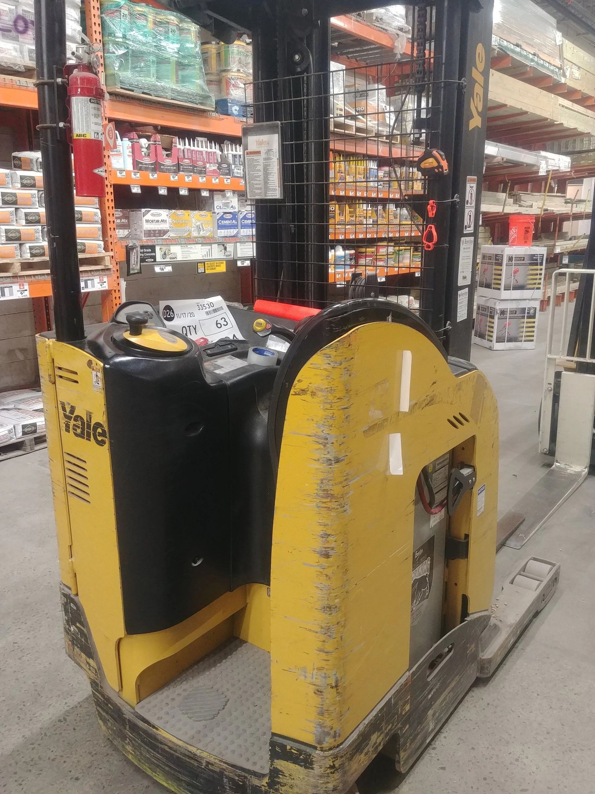 Yellow Yale stand-up forklift inside a store with shelves stocked with merchandise.