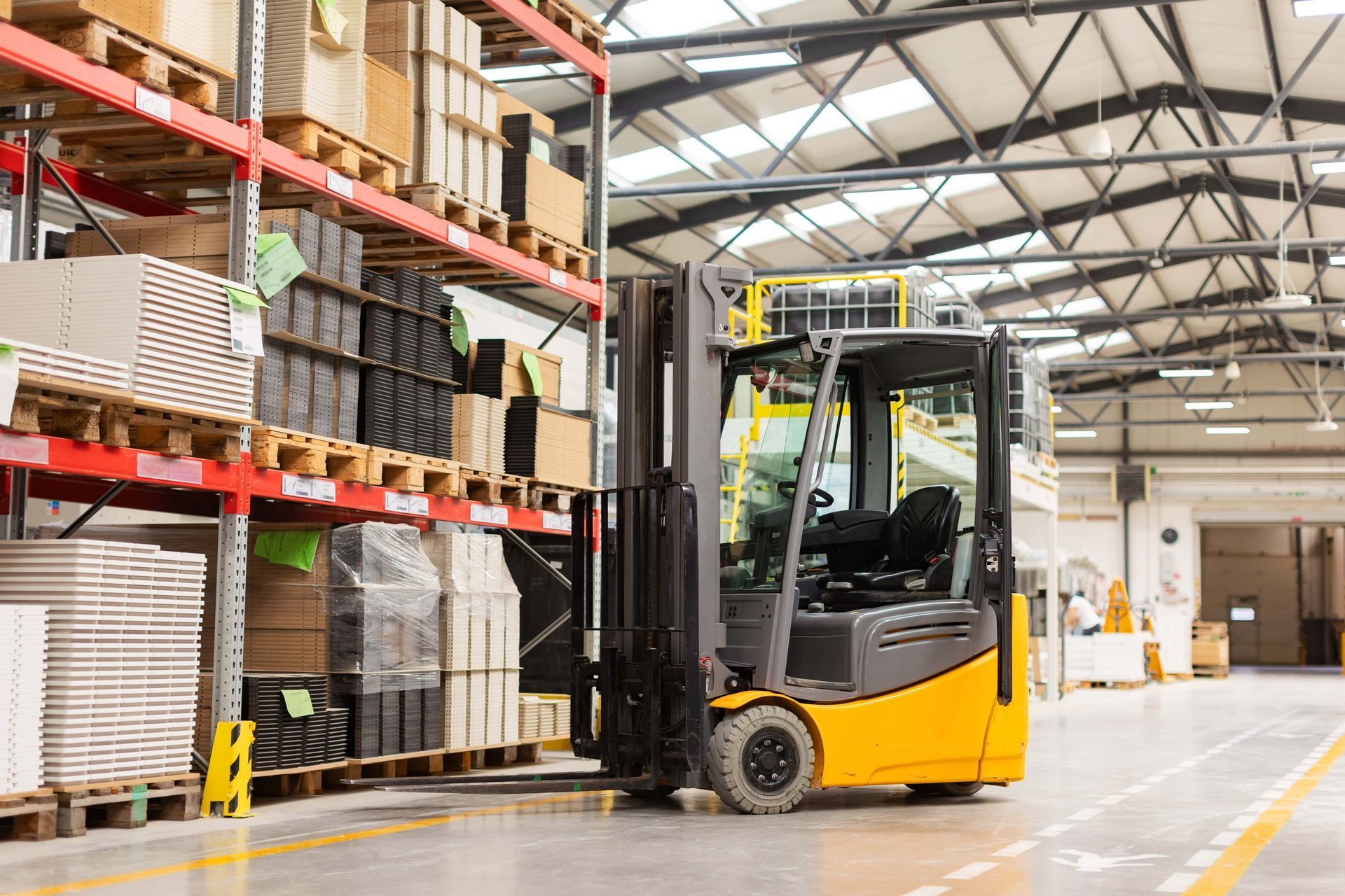 Yellow forklift in warehouse, lifting a pallet of boxes next to shelves filled with goods.