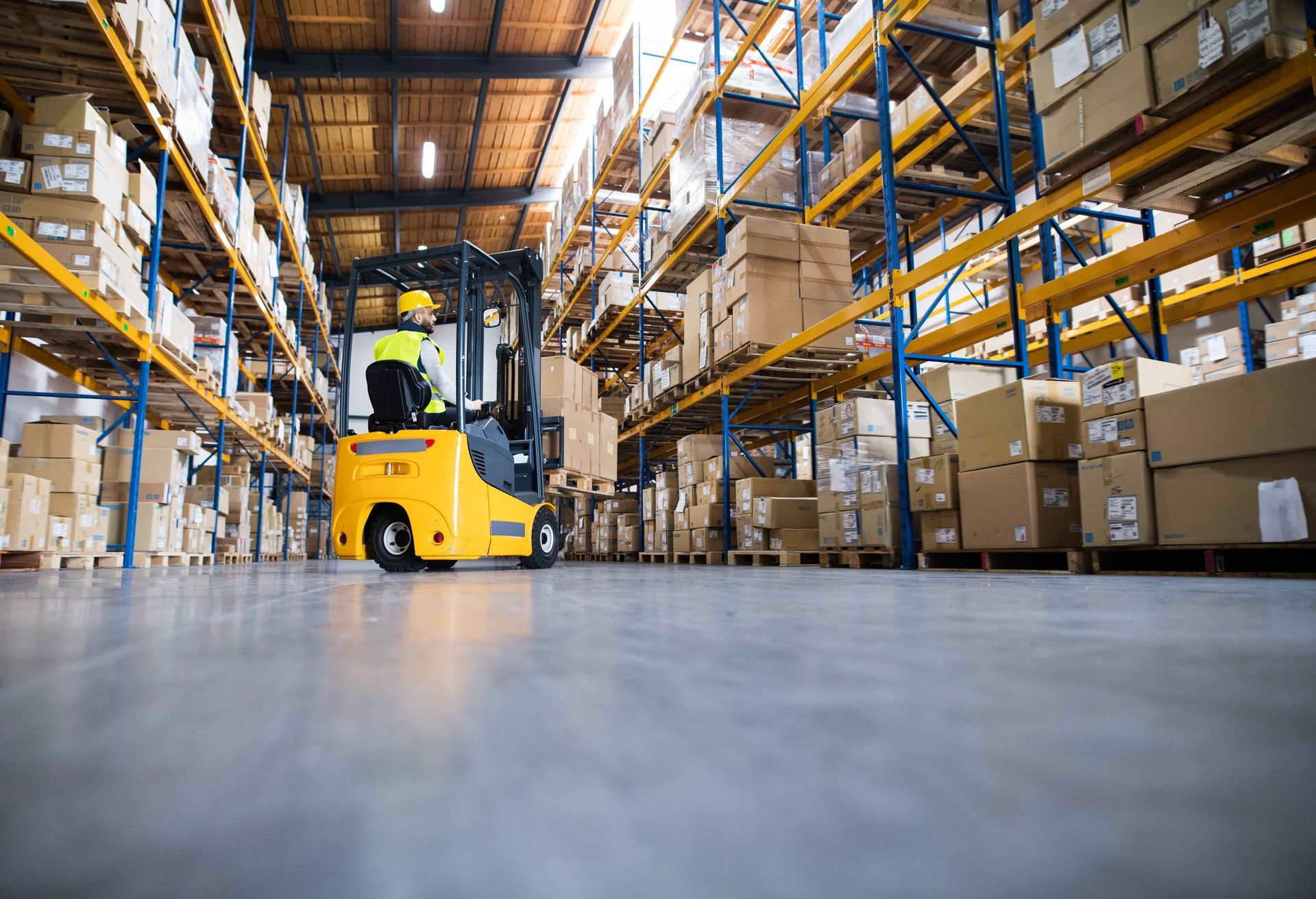 Forklift operator in a warehouse, surrounded by shelves stacked with cardboard boxes.
