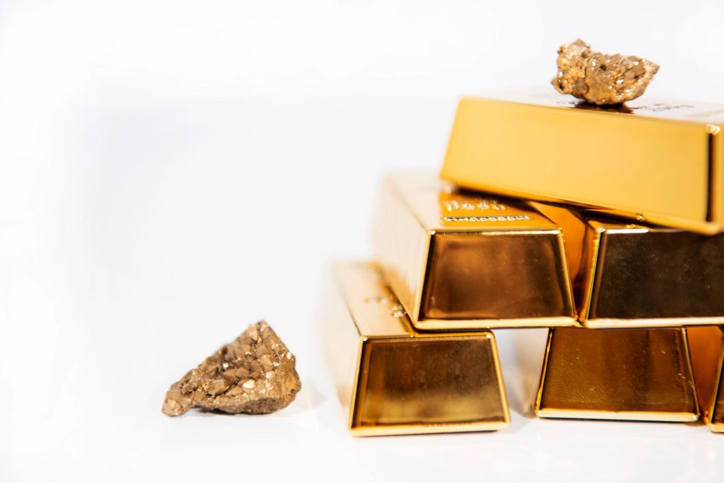 Lingotti d’oro impilati con piccole pepite su sfondo bianco