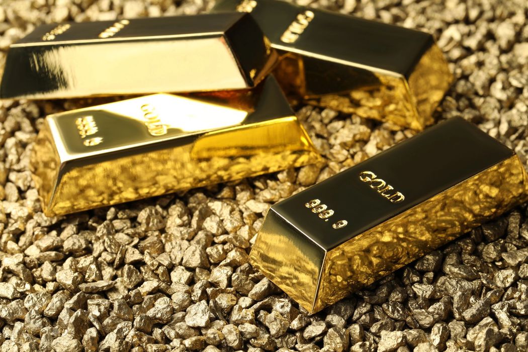 Lingotti d’oro adagiati su un letto di pepite d’oro, scintillanti sotto una luce calda.