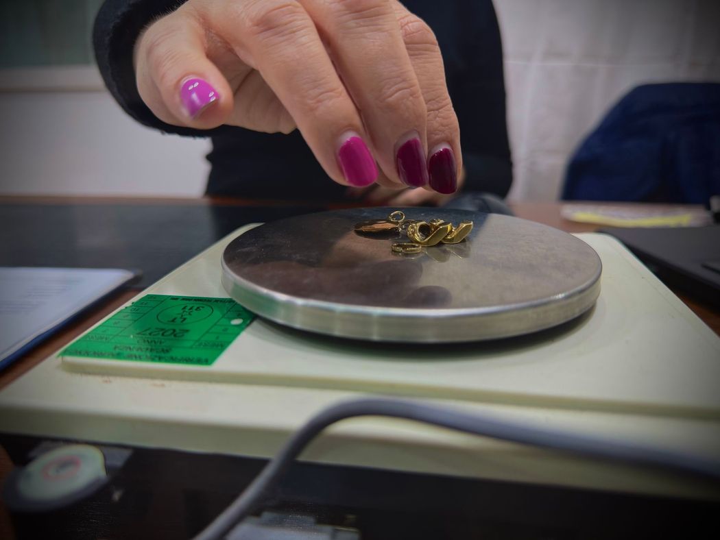 Una mano deposita piccoli oggetti d’oro su una bilancia digitale per gioielli con un’etichetta dal display verde