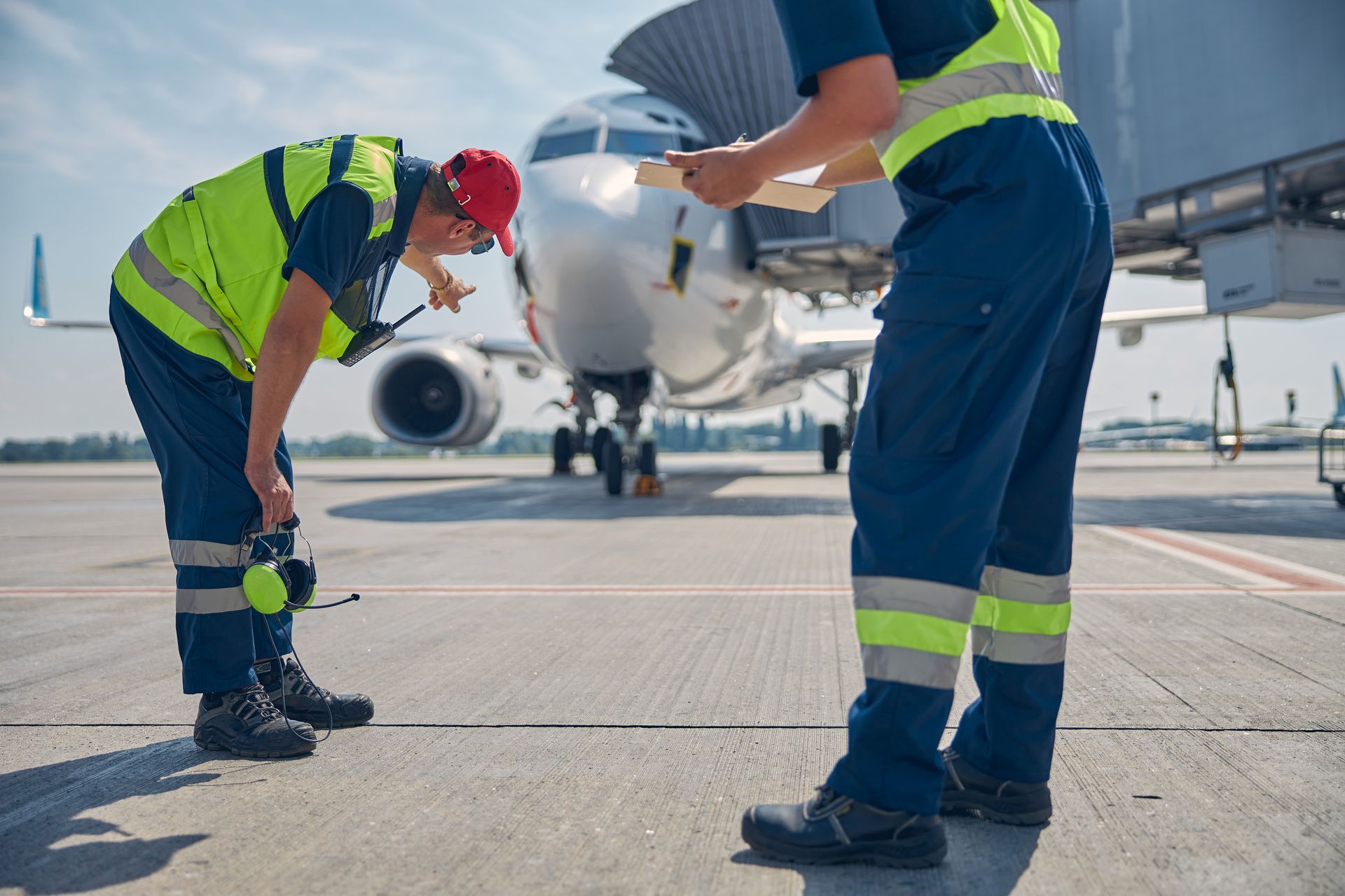 Two airport ground crew in high-visibility vests inspect a jet on the tarmac.