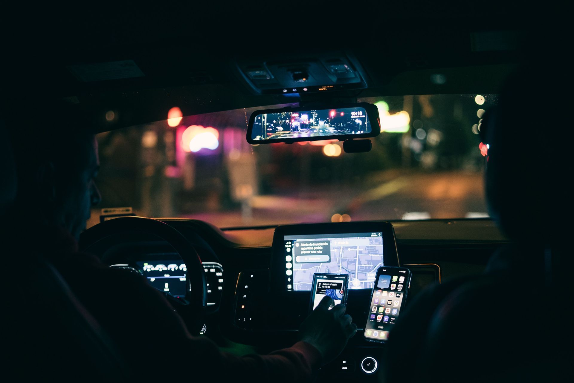 Driver’s view of a car interior at night, with glowing dashboard and navigation screens in traffic.