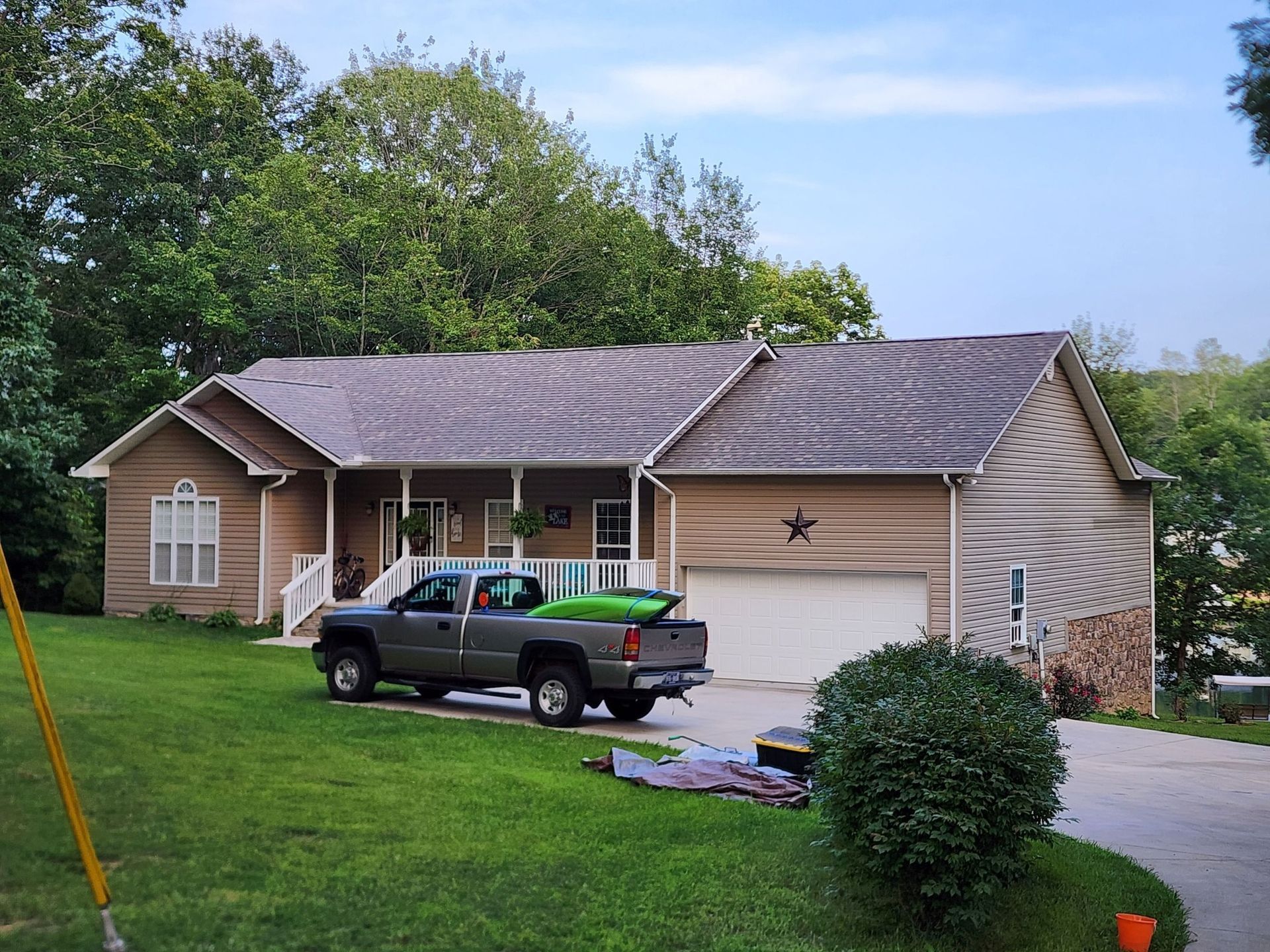 A tan, single-story house with a shingled roof, a front porch, and a gray pickup truck parked in the driveway.