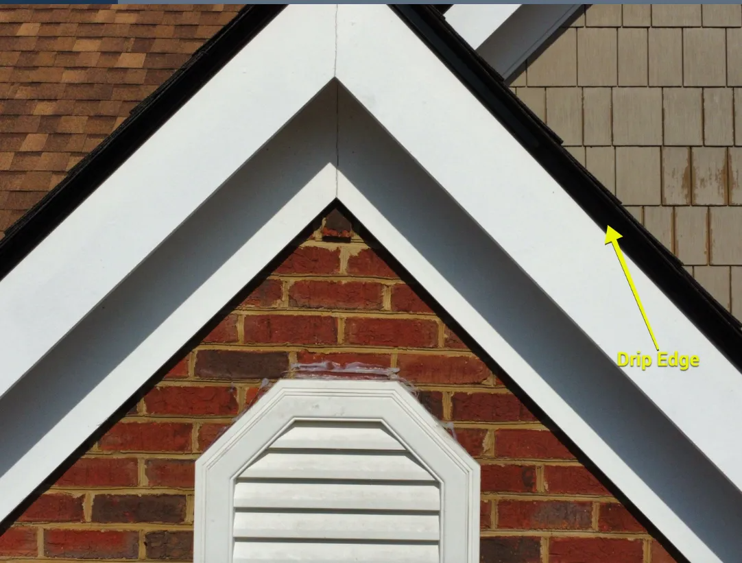 Close-up of a white-trimmed roof gable over a brick wall with an attic vent and a yellow arrow pointing to the drip edge.