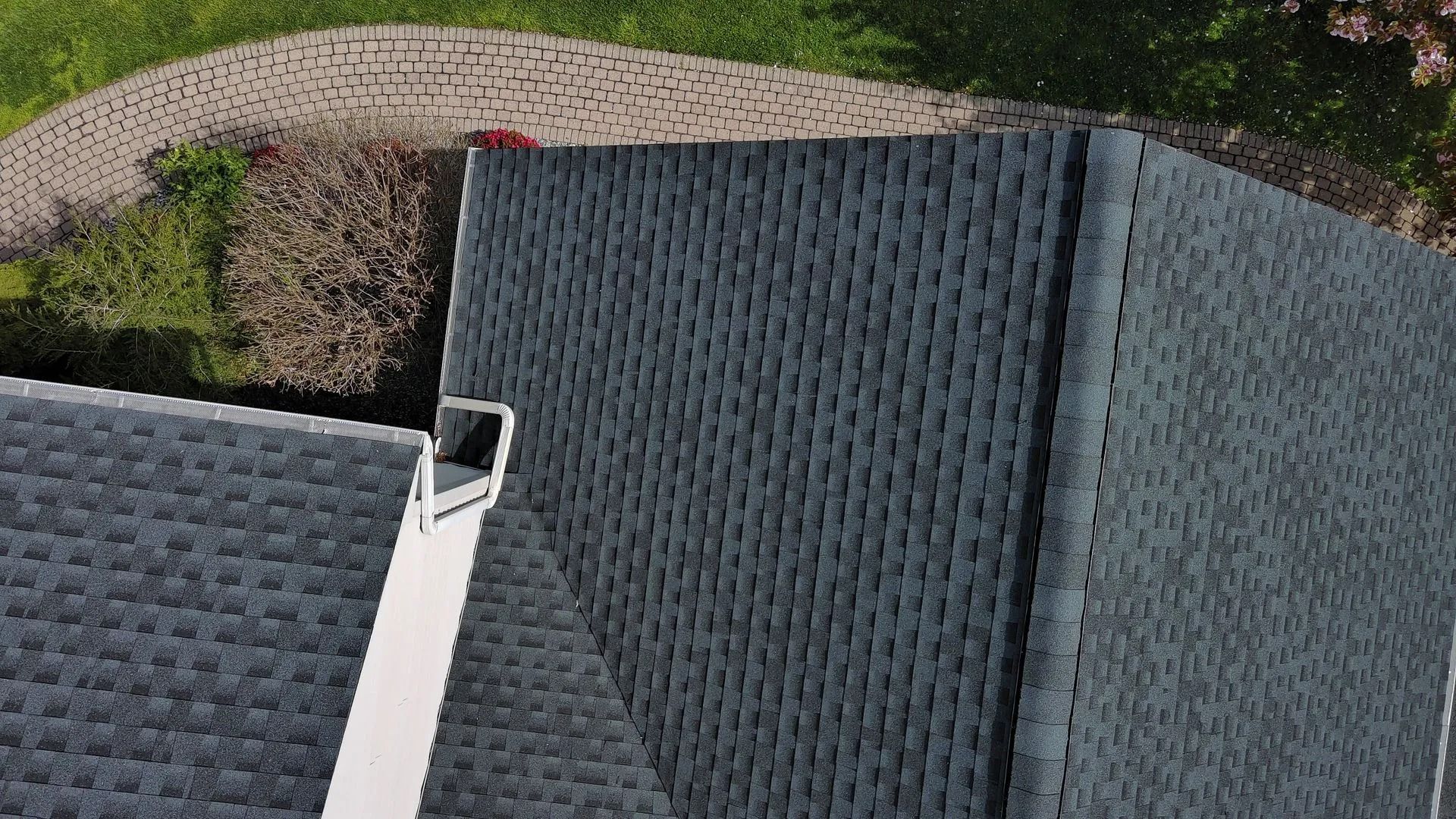 An overhead view of a dark grey asphalt shingle roof with a white metal vent and edge flashing.