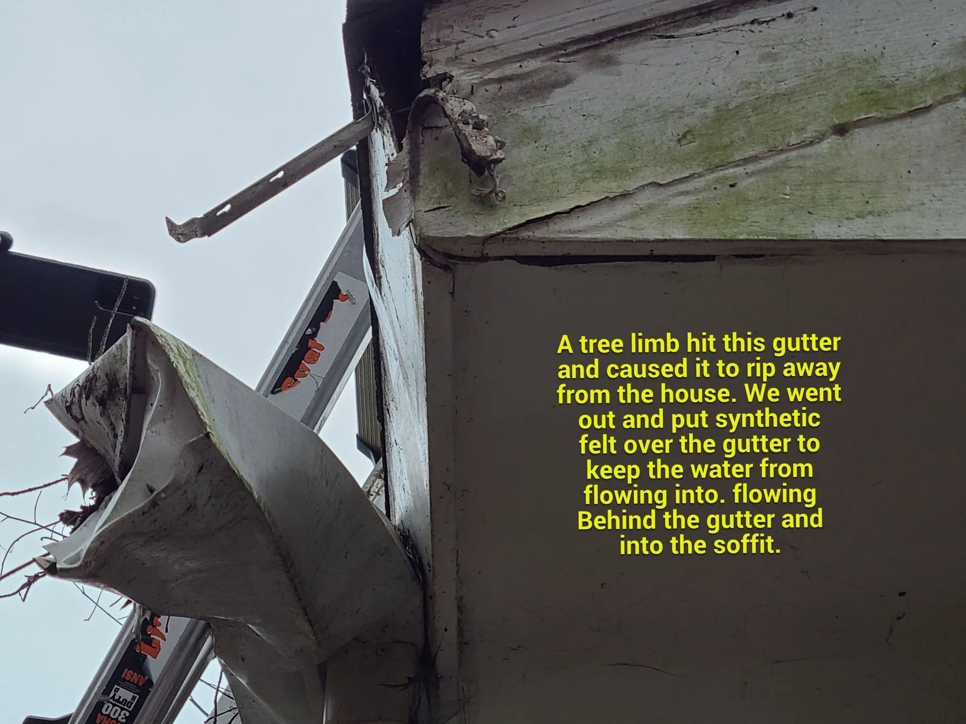 A detached gutter hanging from a house corner, with synthetic felt placed over it to prevent water damage to the soffit.