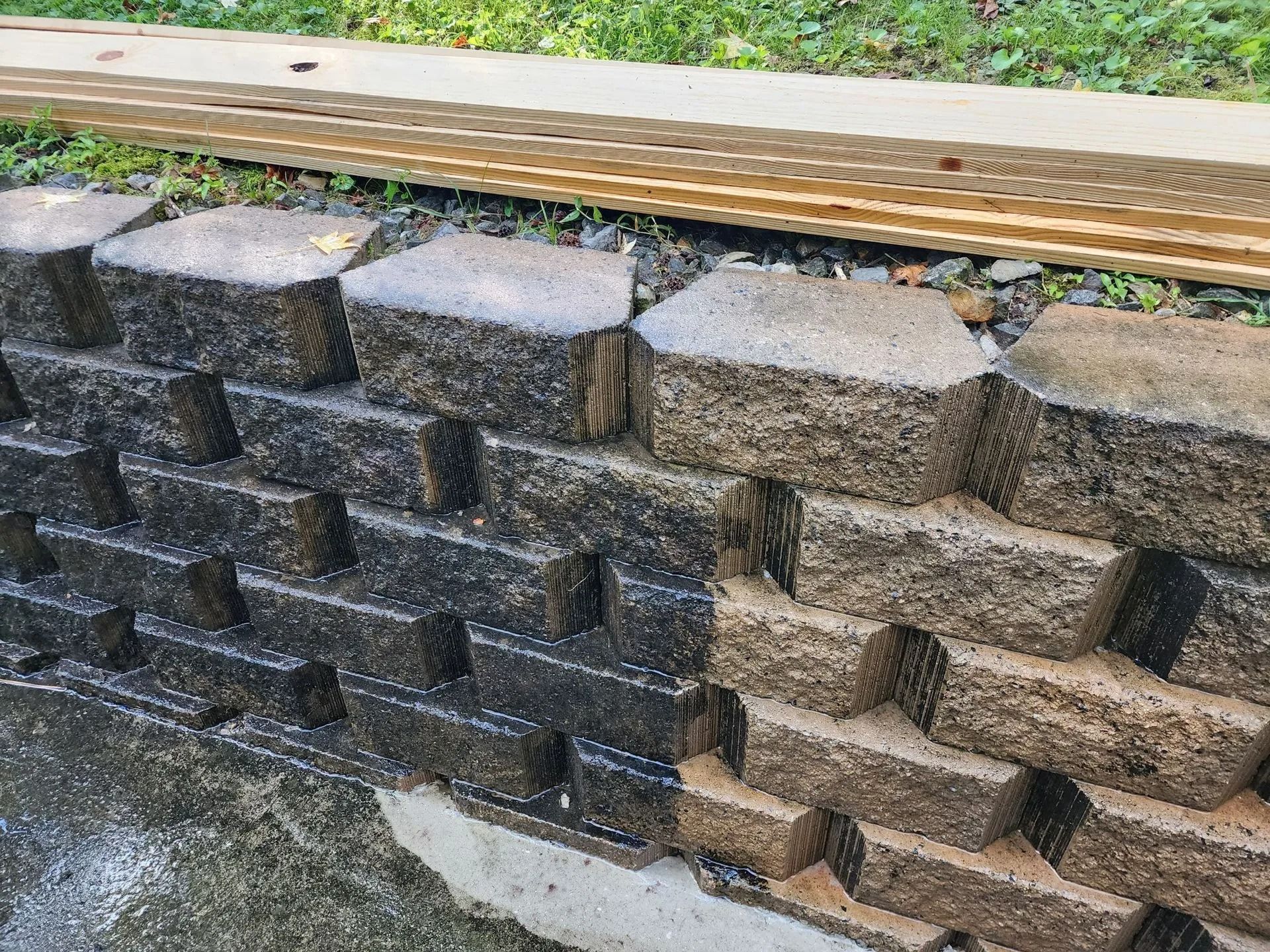 Stacked dark and tan concrete retaining blocks under a wooden beam outdoors