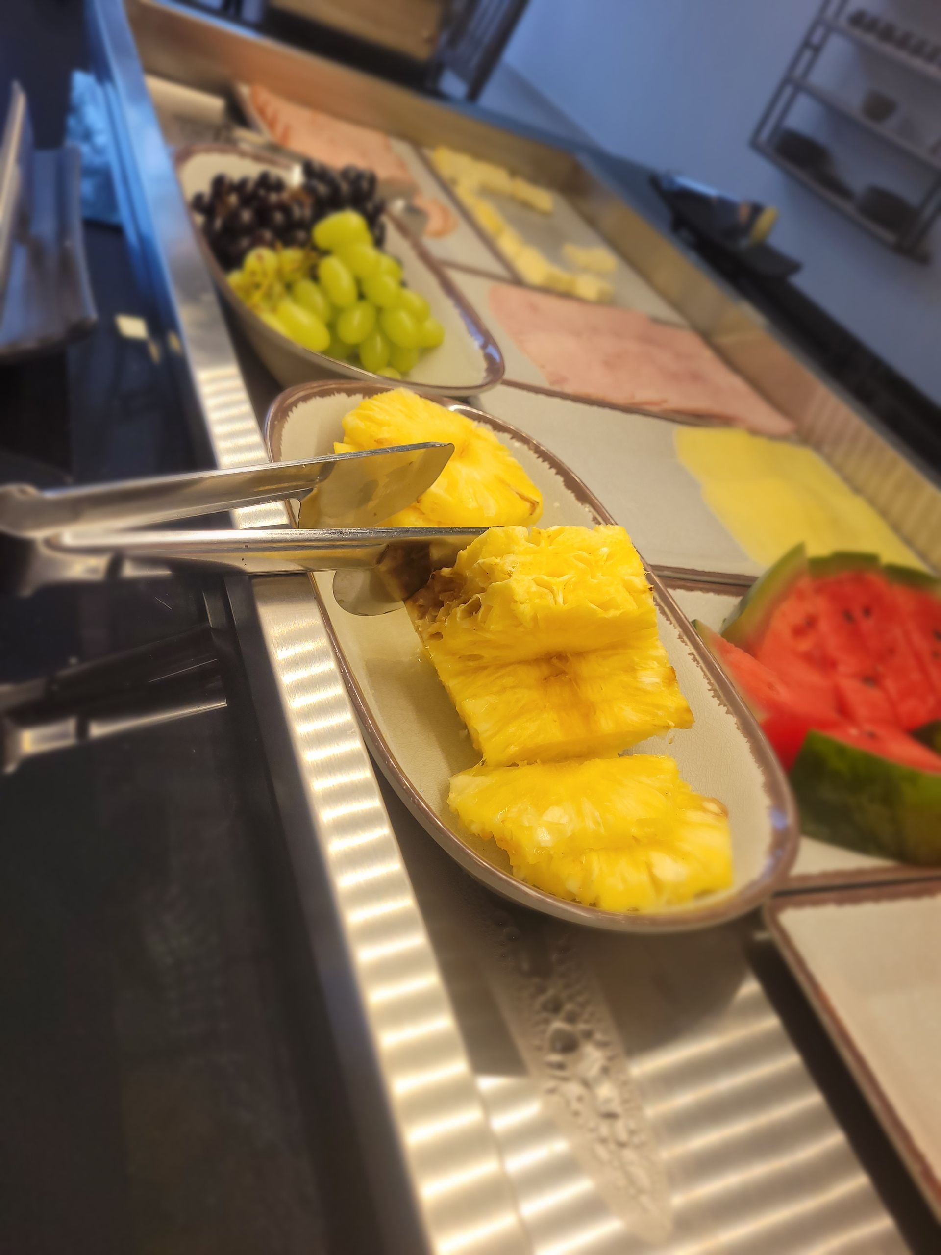 Bandejas de sobremesas em estilo bufê com fatias de abacaxi, uvas, melancia e outras frutas e doces gelados.