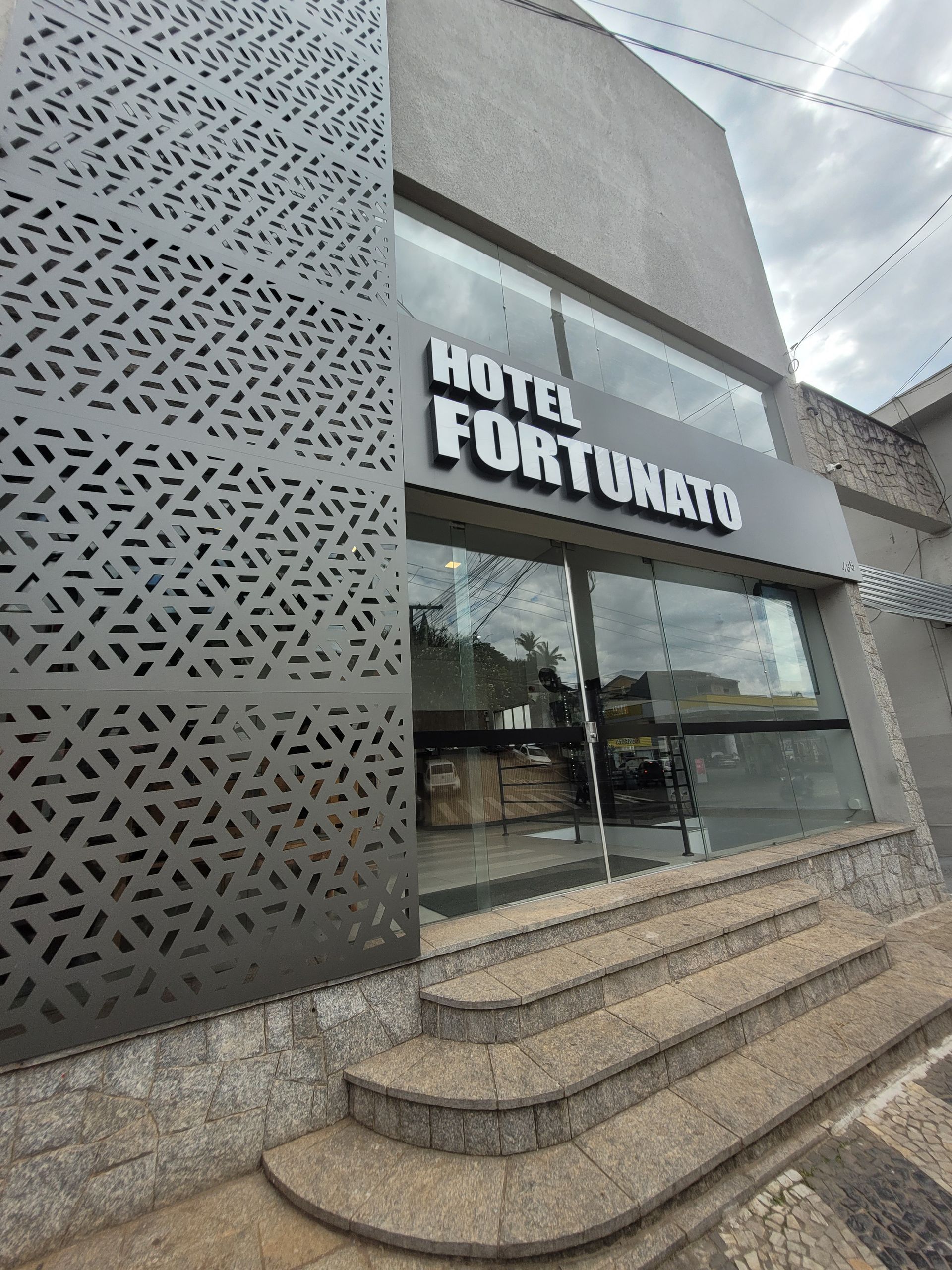 Entrada do Hotel Fortuniato com portas de vidro, fachada com padrões e degraus curvos.