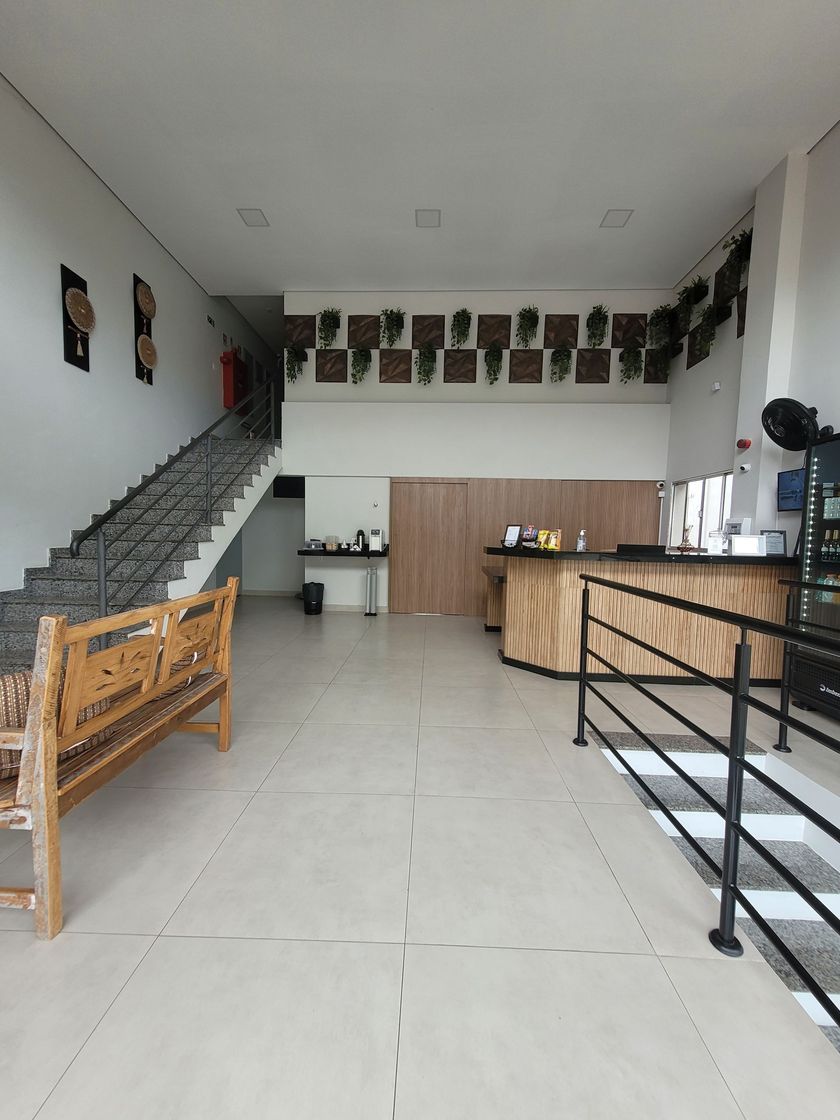 Hall de entrada vazio com escadaria, balcão de recepção de madeira e bancos sobre piso de azulejo.