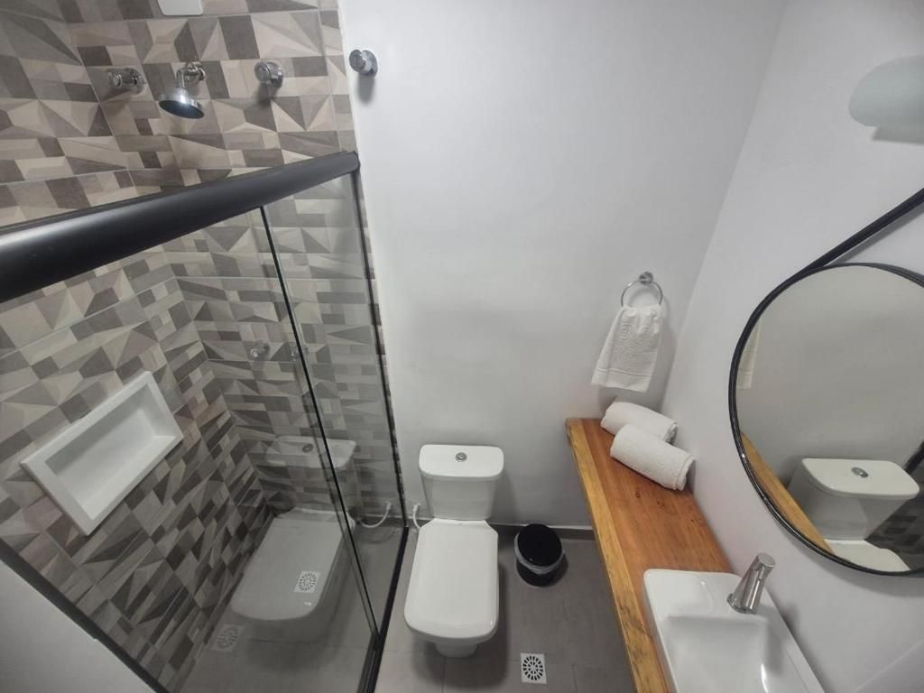 Banheiro pequeno com box de vidro, vaso sanitário, bancada de madeira, pia e porta-toalhas.