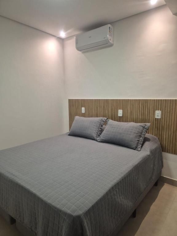 Quarto minimalista com colcha cinza, cabeceira de madeira e ar-condicionado de parede.