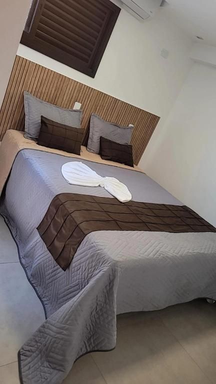 Cama arrumada com roupa de cama cinza e marrom em um quarto pequeno com cabeceira de tijolos à vista.