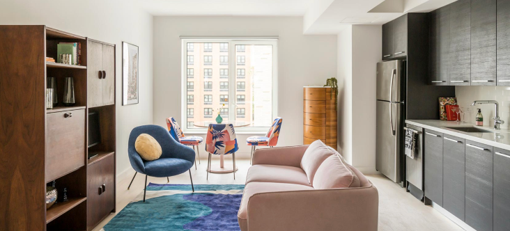 a living room with a pink couch and a blue chair and a kitchen .