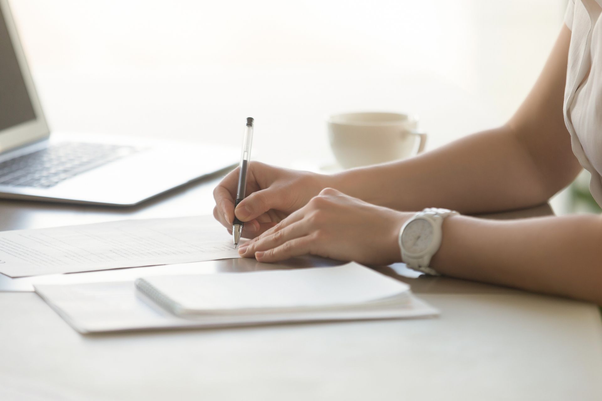 Una mujer está sentada en un escritorio escribiendo en un trozo de papel con un bolígrafo.