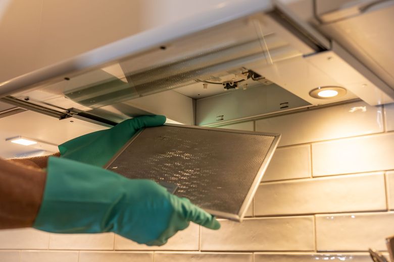 A person wearing green gloves is cleaning a kitchen hood filter.
