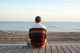 Une personne en pull est assise sur une promenade, face à l'océan, au coucher du soleil.