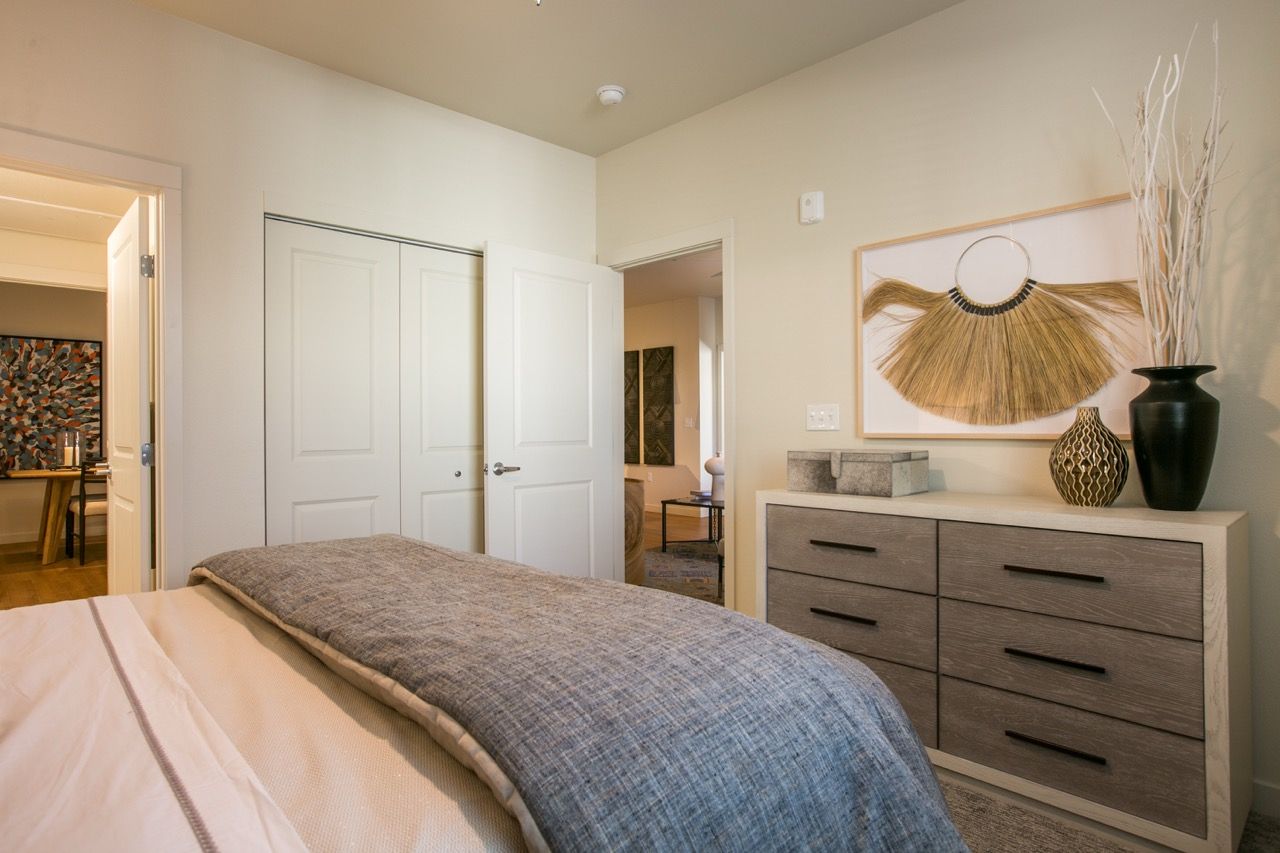 Bedroom with a neatly made bed, a six-drawer dresser, and doorway to hallway.