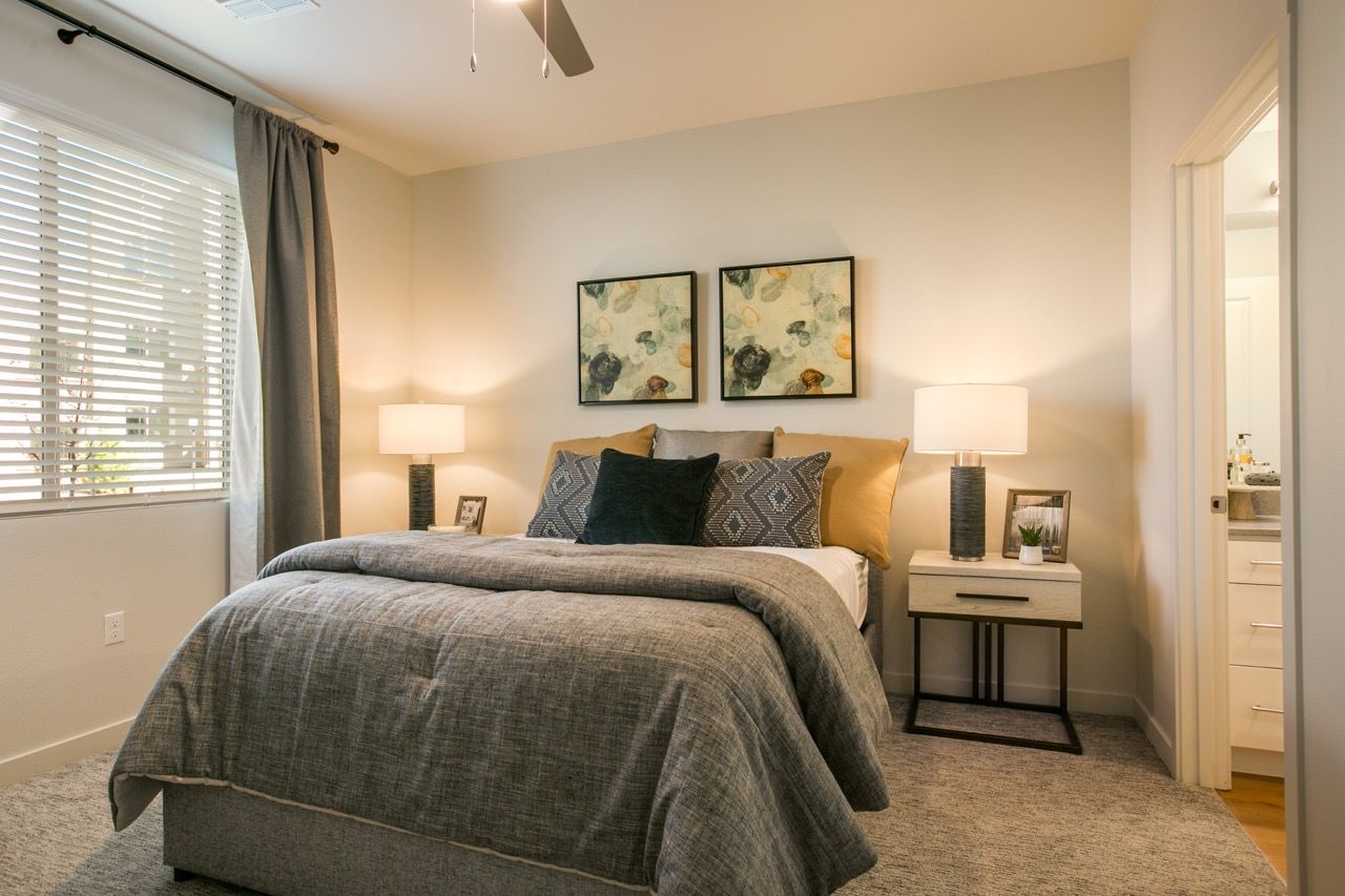 Bedroom in apartment with a queen bed, two nightstands, lamps, and doorway to a bathroom.