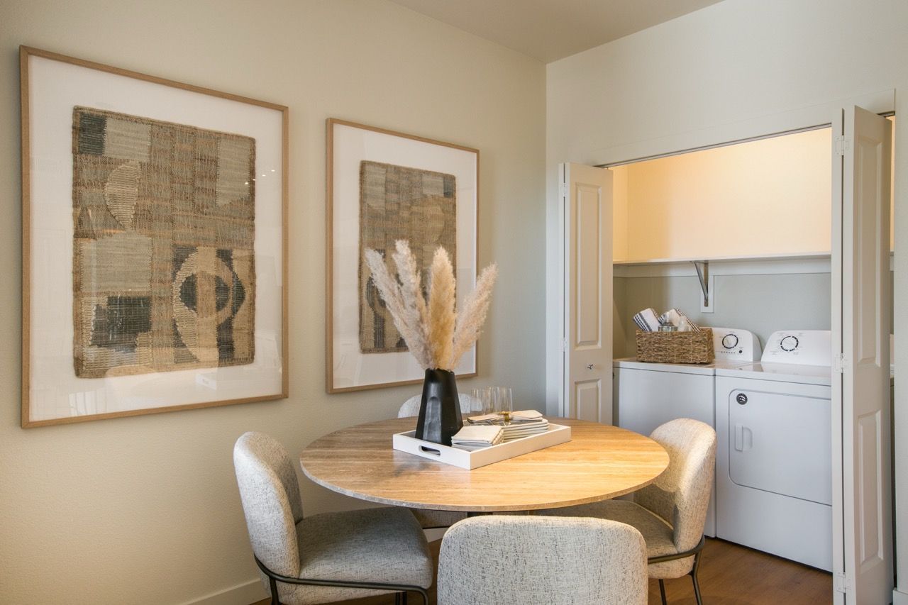Dining nook with a round wood table and cream chairs beside a laundry closet housing a washer and dryer.