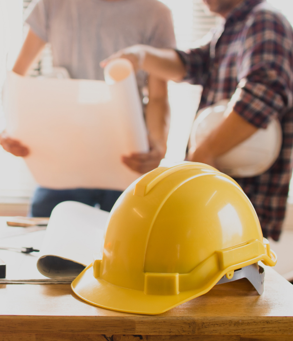 Yellow hard hat on a table with people working in the blurred background