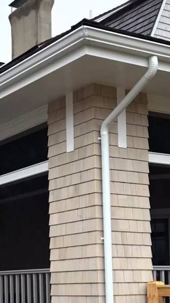 White downspout and gutter on a cream brick house exterior by a porch and roofline.
