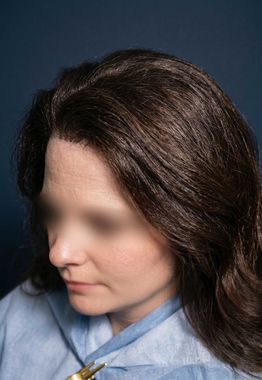 Woman with dark hair in a blue shirt, looking down against a dark background