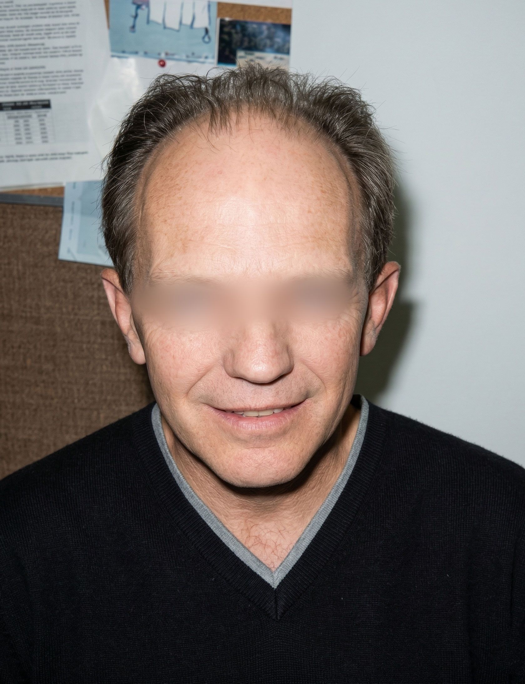 Man indoors against a wall, wearing a black sweater, with a slight smile.