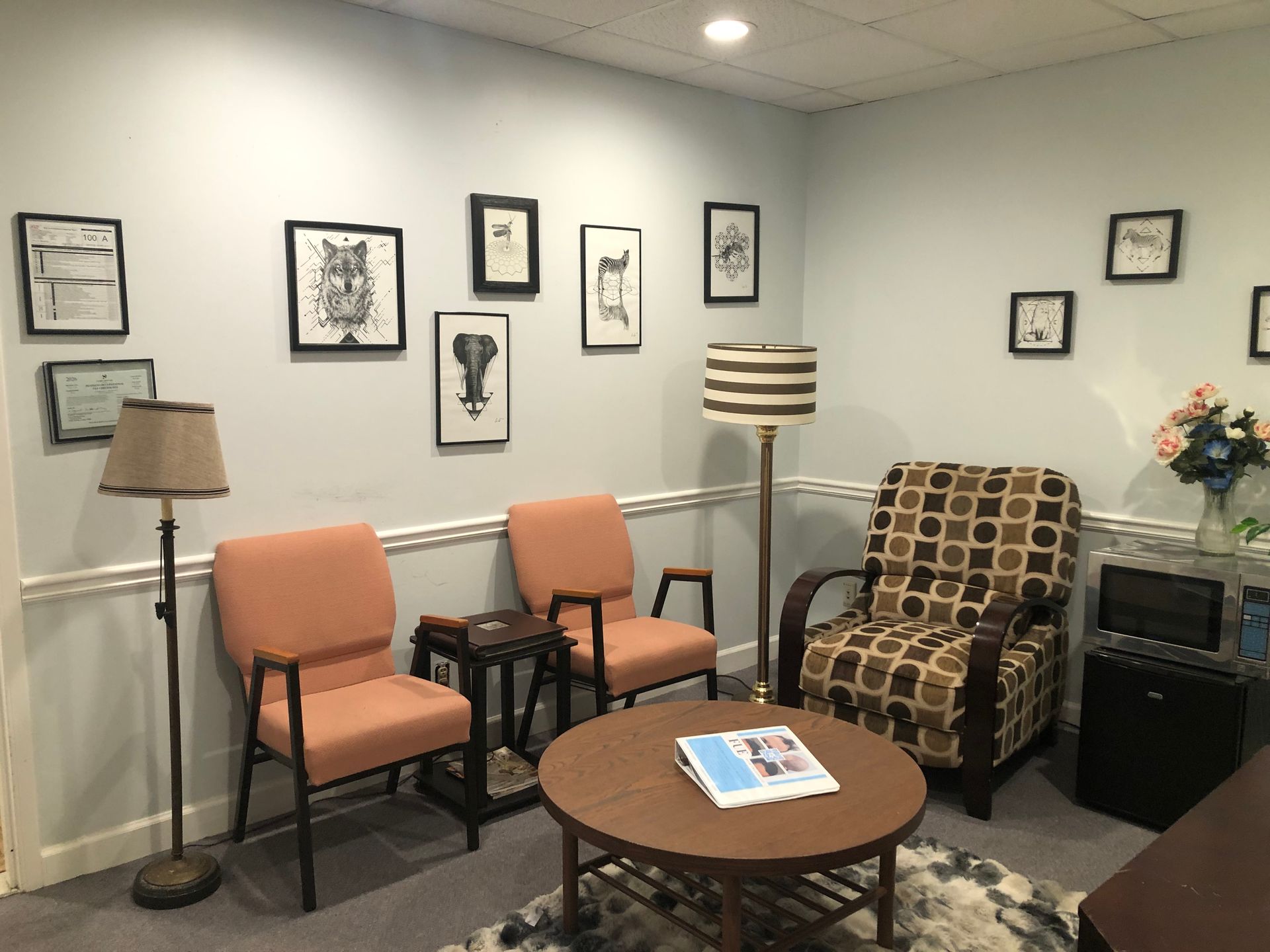 Waiting room with orange chairs, patterned armchair, round table, lamp, and framed wall art.