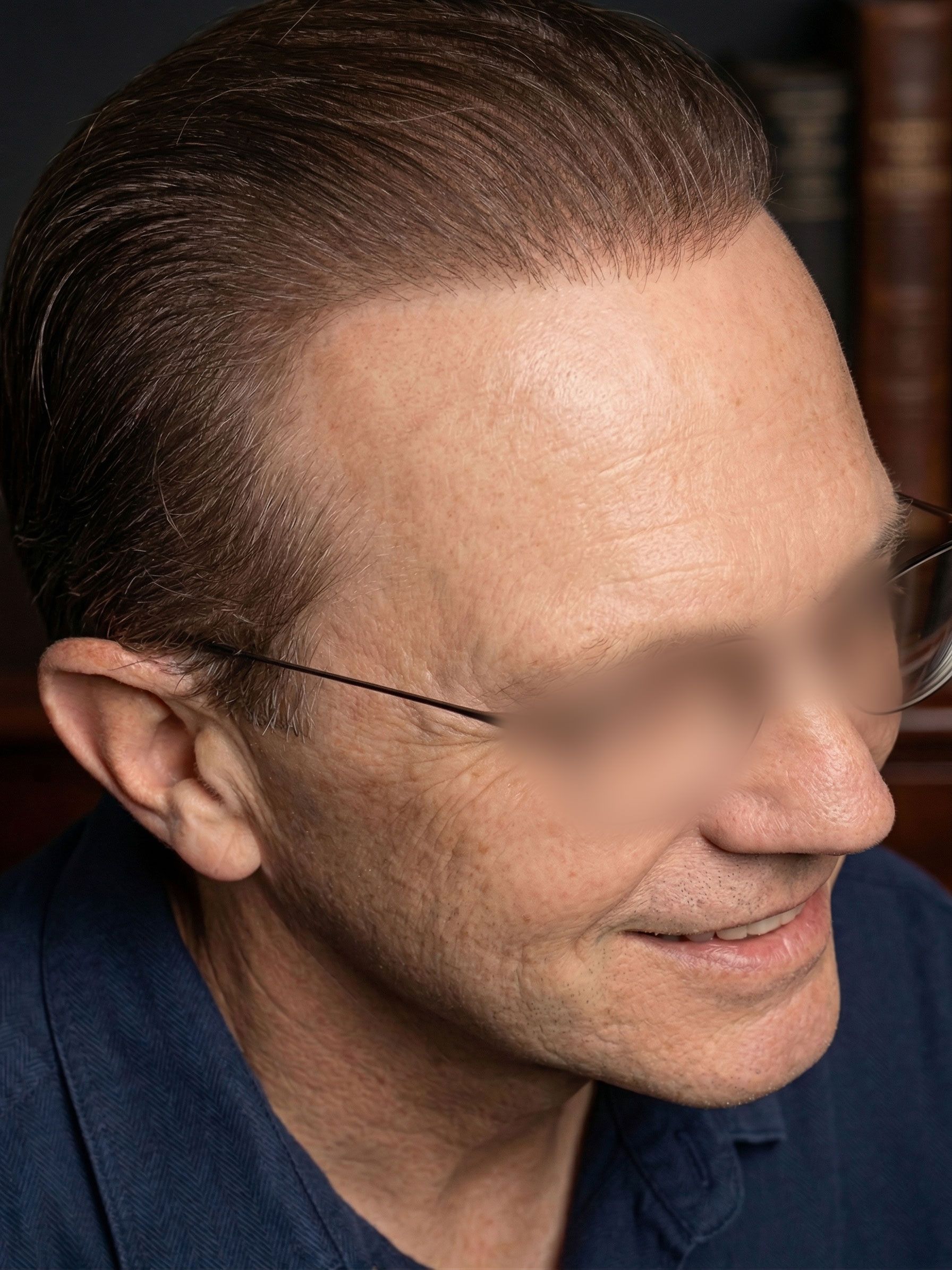 Close-up profile of a man with slicked-back hair, smiling slightly against a dark background