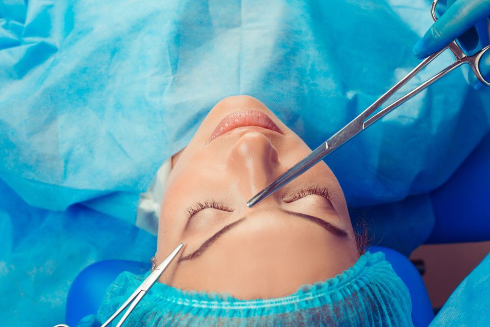 A surgical procedure on the eyelid, with sterile blue drapes, gloves, and metal surgical instruments visible.