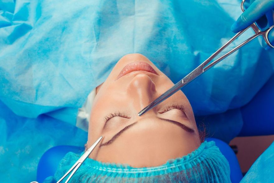 A surgical procedure on the eyelid, with sterile blue drapes, gloves, and metal surgical instruments visible.