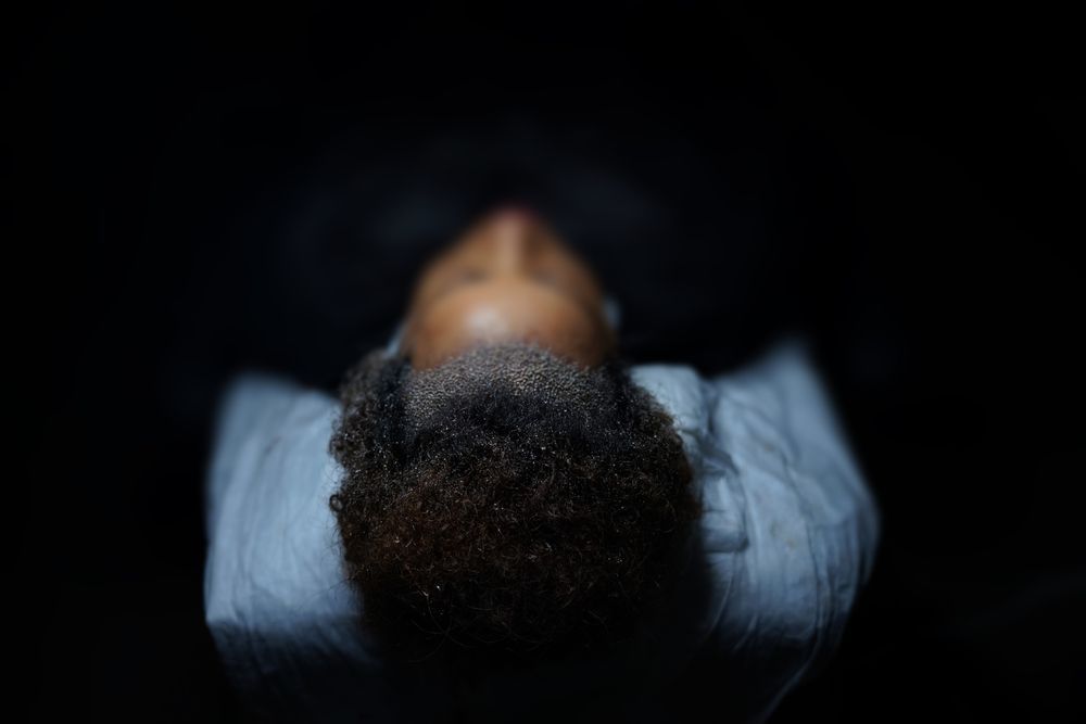 A person with textured hair is lying on a light-colored pillow in a dimly lit, dark setting.