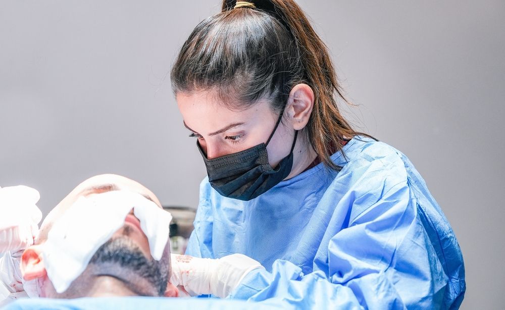 A healthcare professional wearing a blue surgical gown and black mask performing a medical procedure on a patient.
